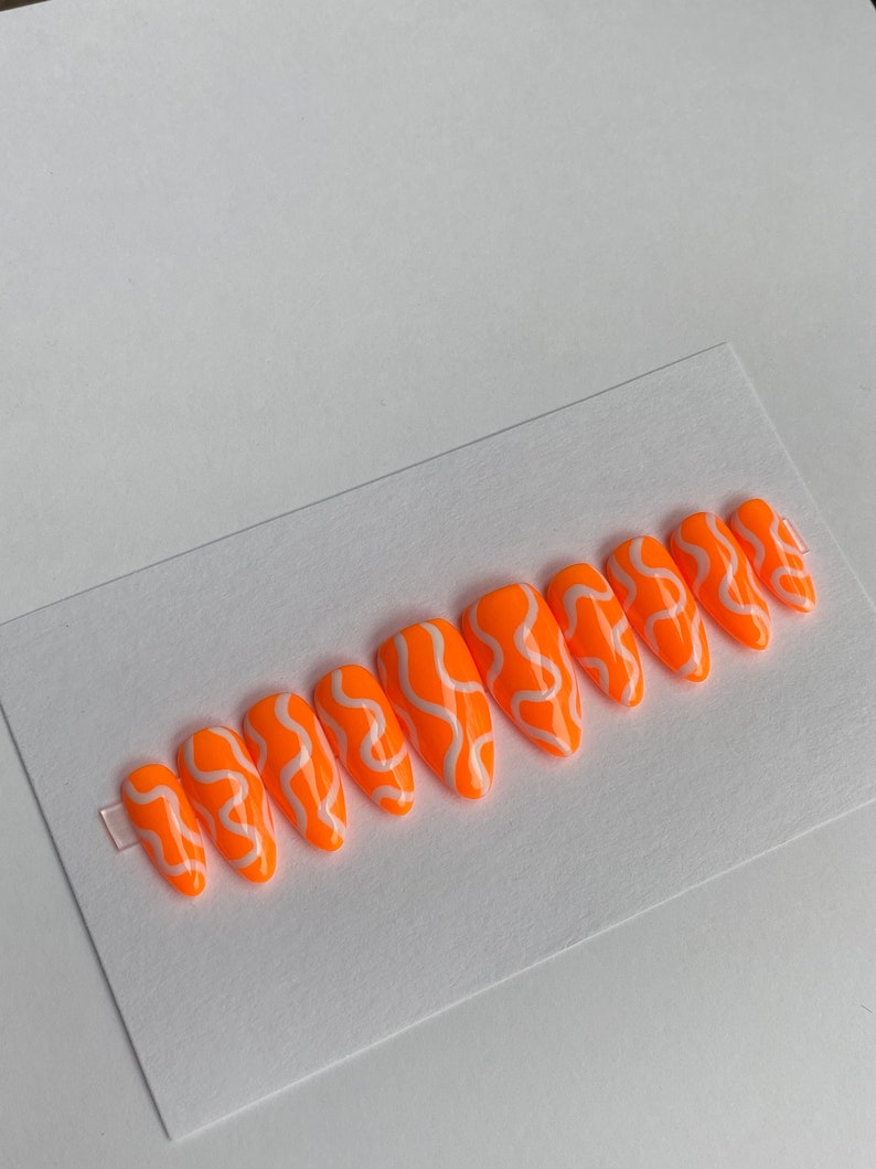 May include: Set of ten orange press-on nails with white abstract swirl designs.