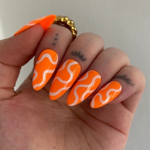 May include: Orange and white swirl patterned press-on nails. The nails are long and have a pointed shape.