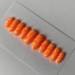 May include: Set of ten orange and white press-on nails with a wavy design.