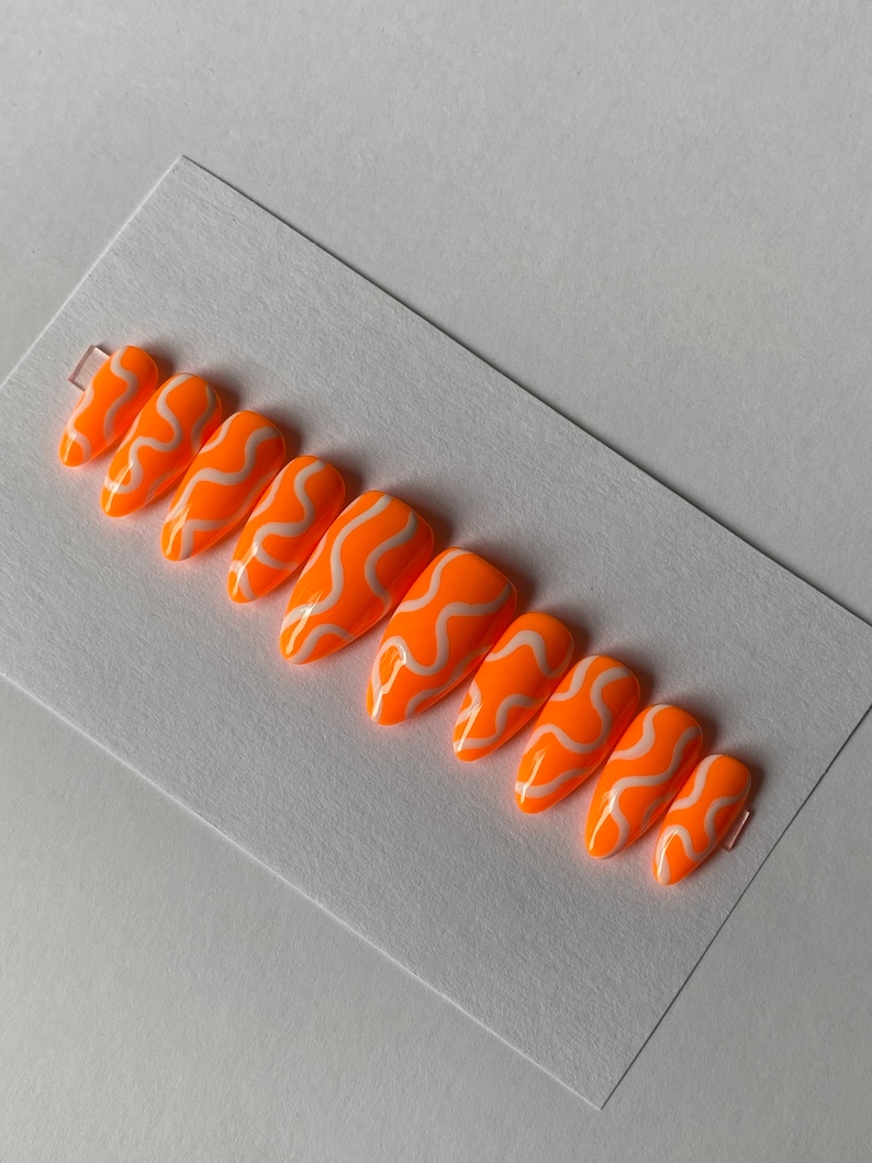 May include: Set of ten orange and white press-on nails with a wavy design.