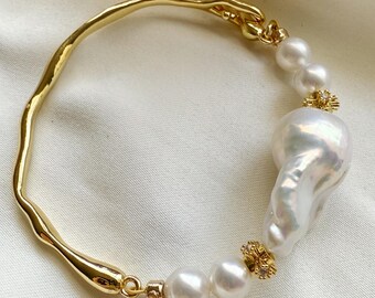 May include: A gold-toned bracelet featuring a large, irregular white pearl and several smaller, round white pearls. The bracelet has a textured, organic design and is accented with small gold-colored embellishments.