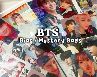Op de afbeelding: Een verzameling fotokaarten met leden van de K-pop-groep BTS. De kaarten zijn in willekeurige volgorde gerangschikt en tonen verschillende afbeeldingen van de bandleden. De kaarten zijn gelabeld met de tekst "BTS Bias/Mystery Bags".
