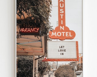 May include: A framed print featuring a vintage motel sign in Austin, Texas. The sign is orange and reads "AUSTIN MOTEL." A neon "VACANCY" sign is visible, along with a sign that says "LET LOVE IN."