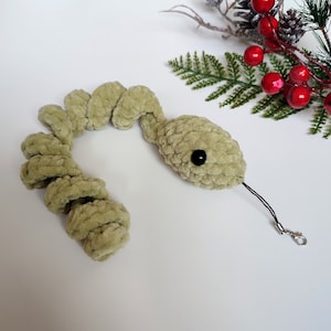 May include: A green crocheted snake with a black eye and a black string attached to a silver clasp.