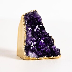 May include: A purple amethyst crystal cluster with a gold-plated base. The crystal is a natural formation with many points and facets.