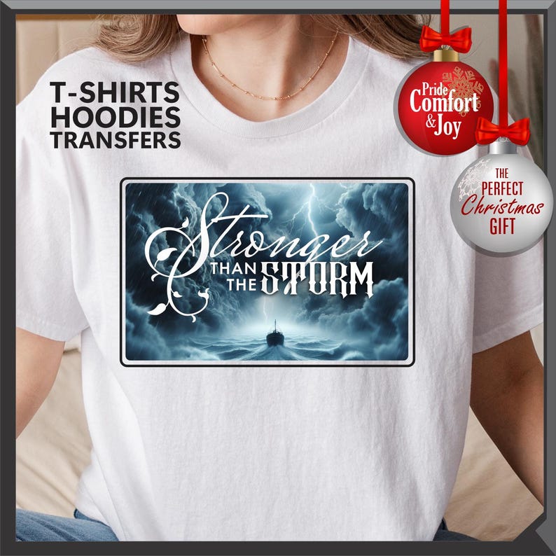 K&ouml;nnte beinhalten: Wei&szlig;es T-Shirt mit einem rechteckigen Grafikmotiv, das eine st&uuml;rmische Ozeanszene und den Text "Stronger Than The Storm" zeigt. Das Shirt hat auch den Text "T-SHIRTS HOODIES TRANSFERS" und weihnachtliche Ornamente.