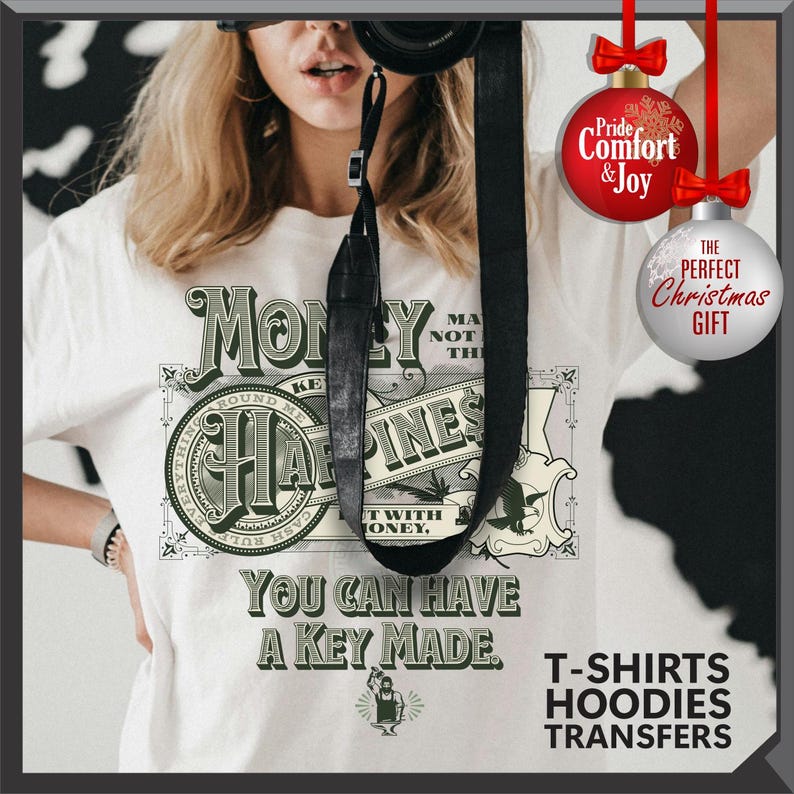 Pu&ograve; includere: T-shirt bianca con grafica verde e nera a forma di banconota, con le scritte "Money Can't Buy Happiness" e "You Can Have A Key Made." L'immagine include anche decorazioni natalizie con testo.