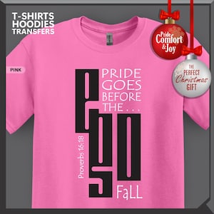 May include: A pink t-shirt with the text "PRIDE GOES BEFORE THE...FALL" in black. The shirt also features the text "Proverbs 16:18" in white. The image includes Christmas ornaments with the text "Pride Comfort & Joy" and "The Perfect Christmas Gift."