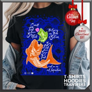Pu&ograve; includere: Maglietta nera con sfondo blu e illustrazioni di pesci. La maglietta presenta il testo "Small Fish have Big Fish, Big Fish have Bigger Fish, and so on ad infinitum." Sono visibili anche due decorazioni natalizie.