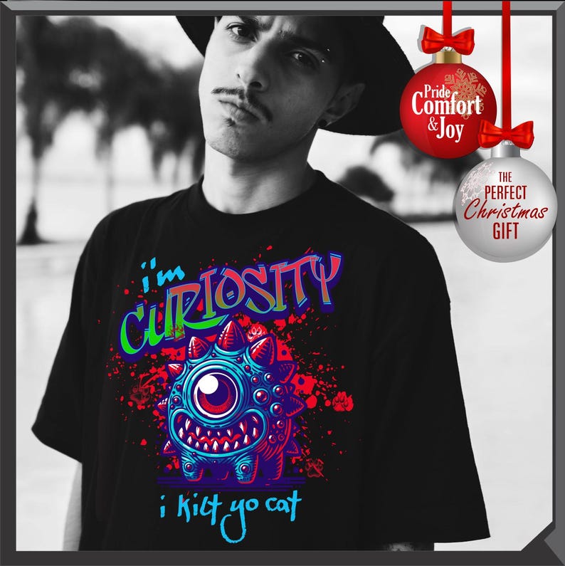 Może przedstawiać: Czarna koszulka z kolorową grafiką jednookiego potwora i napisem "I'm Curiosity i kilt yo cat". Projekt zawiera niebieskie, czerwone i fioletowe akcenty. Obraz zawiera ozdoby świąteczne.