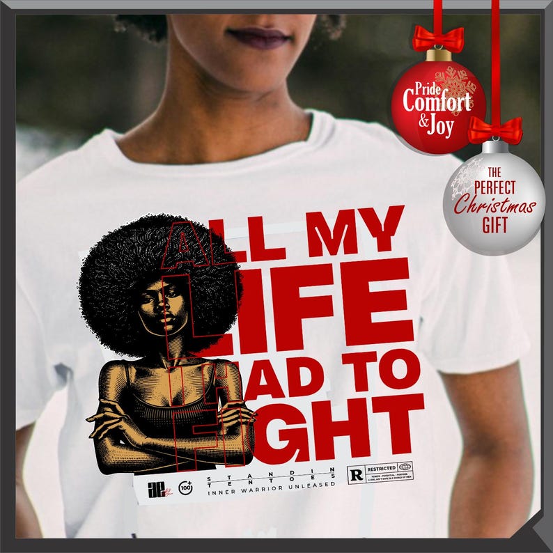 Może przedstawiać: Biała koszulka z grafiką kobiety z afro i napisem "ALL MY LIFE HAD TO FIGHT" w kolorze czerwonym. Koszulka zawiera r&oacute;wnież napis "INNER WARRIOR UNLEASHED". Ozdoby świąteczne w tle.