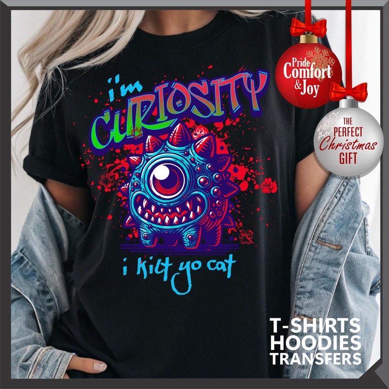 Może przedstawiać: Czarny t-shirt z kresk&oacute;wkowym potworem w kolorze niebieskim, czerwonym i zielonym. Tekst na koszulce brzmi "I'm Curiosity, i kilt yo cat". Zawiera grafikę ozd&oacute;b świątecznych z napisem "The Perfect Christmas Gift".