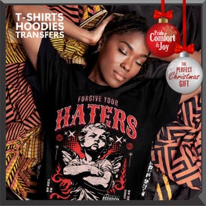 May include: Black t-shirt with the text "FORGIVE YOUR HATERS" in red and white, featuring an angel graphic. The image includes text that says "T-SHIRTS HOODIES TRANSFERS". Decorative Christmas ornaments with text are also present.