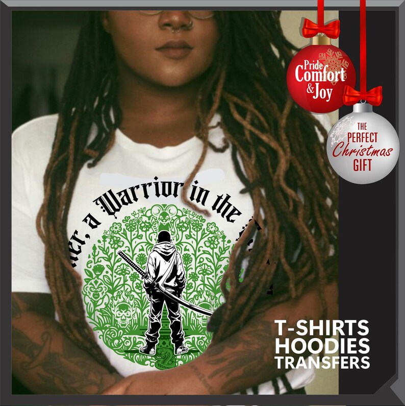 May include: White t-shirt with a green and black graphic of a warrior holding a sword, surrounded by floral and skull designs. Text on the shirt reads "Warrior in the". The image also includes Christmas ornaments and text promoting t-shirts, hoodies, and transfers.