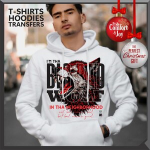 Op de afbeelding: Witte hoodie met een afbeelding van een grommende wolf in rood en zwart, met de tekst "I'M THA BIG BAD WOLF" en "IN THA NEIGHBORHOOD". De hoodie heeft ook de tekst "T-SHIRTS HOODIES TRANSFERS".