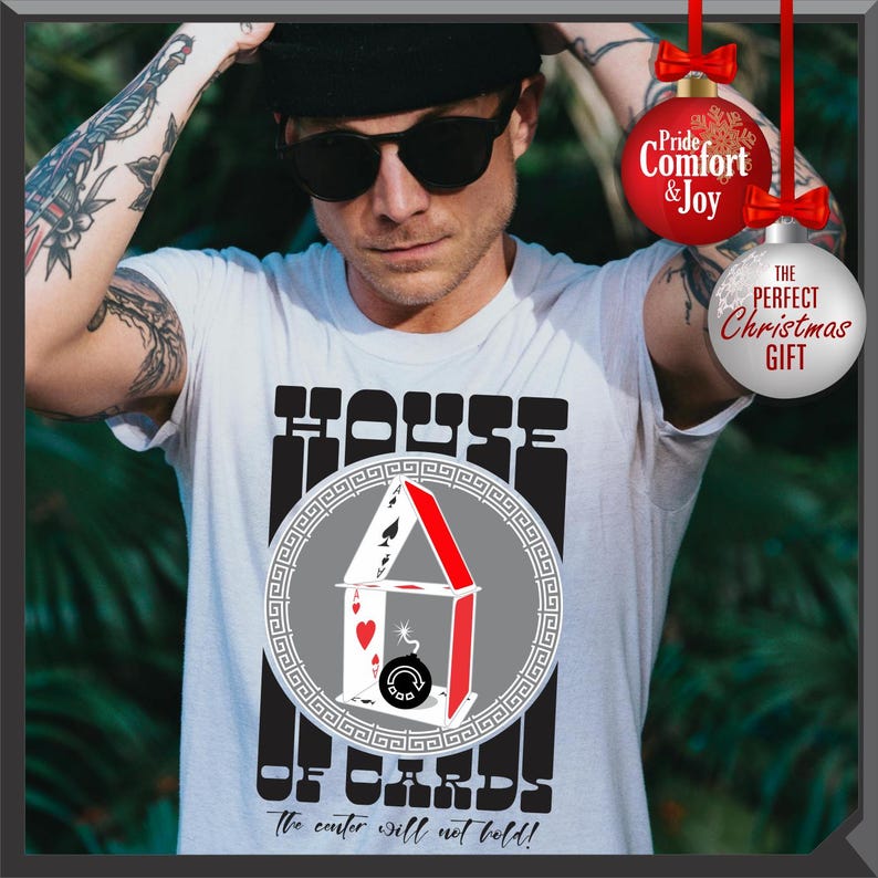 May include: White t-shirt with a graphic of a house made of playing cards, with the text "HOUSE OF CARDS" and "The center will not hold!". The design includes a red, white, and black color scheme. The shirt is a perfect Christmas gift.