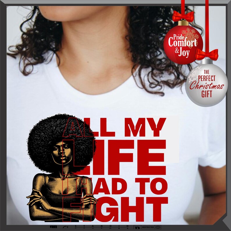 Może przedstawiać: Biała koszulka z grafiką kobiety z afro i czerwonym napisem "ALL MY LIFE HAD TO FIGHT". Dwie bombki choinkowe wiszą u g&oacute;ry po prawej stronie, jedna czerwona z napisem "Pride & Joy", a druga srebrna z napisem "THE PERFECT CHRISTMAS GIFT".