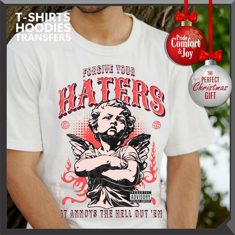 May include: White t-shirt with a graphic featuring an angel with crossed arms, the text "FORGIVE YOUR HATERS," and "IT ANNOYS THE HELL OUT 'EM." The design includes red accents and a parental advisory warning. The image also includes Christmas ornaments.