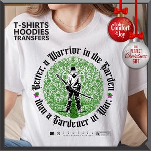 May include: White t-shirt with a graphic featuring a figure with a sword inside a green floral design. Text reads "Better, a Warrior in the Garden than a Gardener at War." Includes text "T-SHIRTS HOODIES TRANSFERS".
