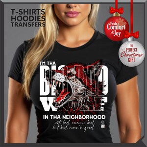 Op de afbeelding: Zwart T-shirt met een rode en witte wolfafbeelding. De tekst "I'M THA BIG BAD WOLF IN THA NEIGHBORHOOD" staat erop. De tekst "not bad mean'in bad but bad mean'in good" is ook zichtbaar.