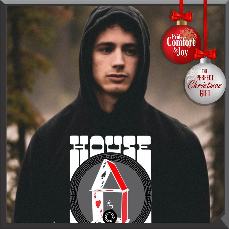 May include: Black hooded sweatshirt with a white "HOUSE" graphic and a playing card house design. The design includes a red roof and a gray background with a Greek key border. The sweatshirt is worn by a person.