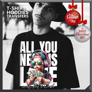Puede incluir: Camiseta negra con el texto "ALL YOU NEED IS LOVE" y un gr&aacute;fico de un ni&ntilde;o con auriculares y gafas de sol, sosteniendo dinero. El texto "well... that's Cash" est&aacute; en la parte inferior. La imagen tambi&eacute;n incluye adornos navide&ntilde;os.