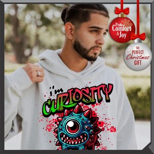 Może przedstawiać: Jasnoszara bluza z kapturem z kolorową grafiką potwora i napisem "I'm Curiosity". Projekt zawiera czerwone, niebieskie i zielone akcenty. Bluza ma kaptur ze sznurkiem i kieszeń typu kangur.