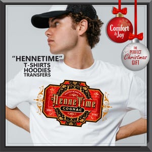 May include: White t-shirt with a cognac label design. The label is red and gold with the words "HenneTime Cognac". The image also includes the text "T-shirts, Hoodies, Transfers". Two Christmas ornaments are in the background.