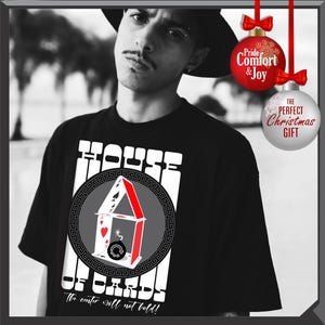 May include: Black t-shirt with a graphic of a house of cards, featuring a red and white design, and the text "HOUSE OF CARDS". The text "The counter will not bold!" is also visible. Two Christmas ornaments are hanging in the background.