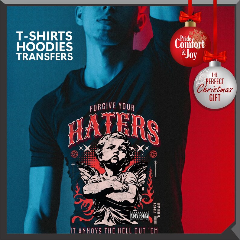 May include: Black t-shirt with the text "FORGIVE YOUR HATERS" and an illustration of an angel with crossed arms. The shirt also has the text "IT ANNOYS THE HELL OUT 'EM" and "ADVISORY". The image includes Christmas ornaments.