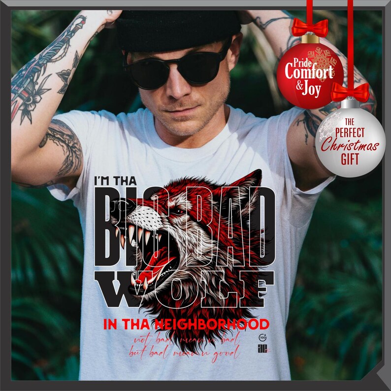 Op de afbeelding: Wit T-shirt met een afbeelding van een grommende rode wolf en de tekst "I'M THA BAD WOLF". Het shirt heeft ook de tekst "IN THA NEIGHBORHOOD" en "THE PERFECT CHRISTMAS GIFT". Een persoon draagt het shirt.