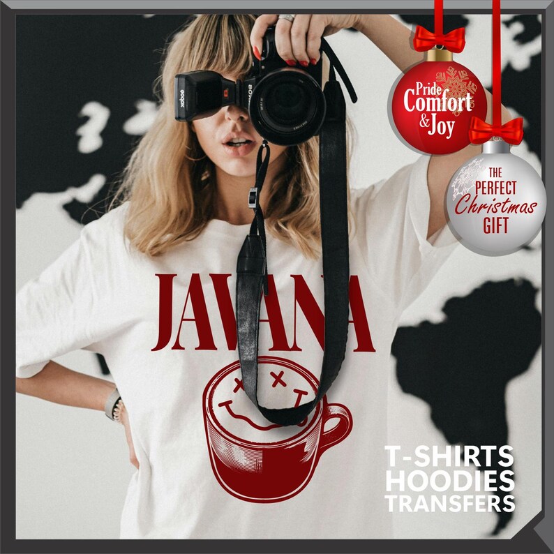 以下が含まれることがあります： バーガンディ色の「JAVANA」の文字と、スマイリーフェイスのバーガンディ色のコーヒーカップのグラフィックが特徴の白いTシャツ。画像には、「Pride, Comfort & Joy」と「The Perfect Christmas Gift」と書かれたクリスマスオーナメントも含まれています。