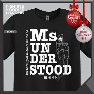 May include: Black t-shirt with the text "Ms Understood" in large white letters. The design includes a hand gesture and the phrase "Oh Lord, please don't let me be." The shirt also has the text "T-SHIRTS HOODIES TRANSFERS" at the top.