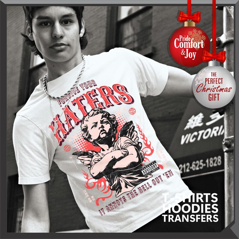 May include: White t-shirt with a graphic featuring the text "FORGIVE YOUR HATERS" in red and a black and red illustration of an angel. The shirt also has the text "IT ANNOYS THE HELL OUT 'EM".