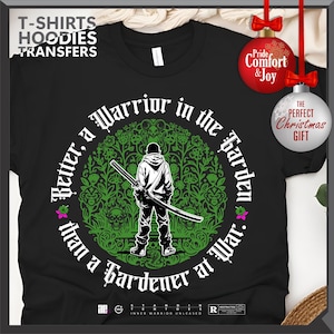 May include: Black t-shirt with a graphic of a person holding a sword, surrounded by a green floral design. Text reads "Better, a Warrior in the Garden than a Gardener at War." Includes the text "T-SHIRTS HOODIES TRANSFERS".