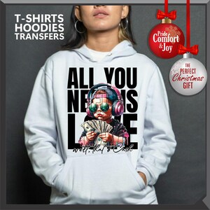 Puede incluir: Sudadera blanca con el texto "ALL YOU NEED IS LOVE" y una ilustraci&oacute;n de un ni&ntilde;o con auriculares y gafas de sol, sosteniendo dinero en efectivo. La sudadera tambi&eacute;n tiene el texto "well, that's cash". La imagen incluye el texto "T-SHIRTS HOODIES TRANSFERS".