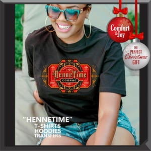May include: Black t-shirt with a HenneTime Cognac label design in red, gold, and black. The image includes text that says "Comfort & Joy" and "The Perfect Christmas Gift". Additional text at the bottom says "HENNETIME" T-SHIRTS HOODIES TRANSFERS.
