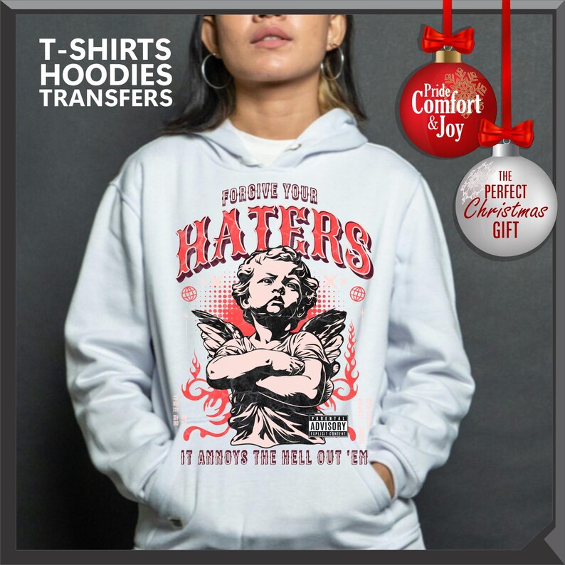 May include: A white hoodie with a graphic featuring an angel, the words "FORGIVE YOUR HATERS," and "IT ANNOYS THE HELL OUT 'EM." The design is in red and black. The image also includes text that says "T-SHIRTS HOODIES TRANSFERS."