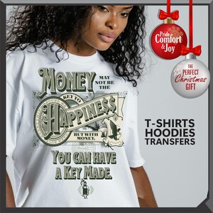 Pu&ograve; includere: T-shirt bianca con un design grafico. Il design presenta la parola "Money" sopra uno striscione che recita "Key to Happiness". Il design include simboli del dollaro e il testo "You Can Have A Key Made". Decorazioni natalizie sullo sfondo.