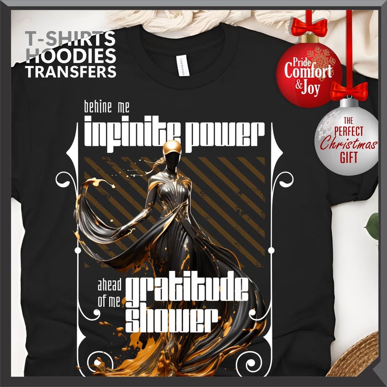 Może przedstawiać: Czarny t-shirt z grafiką postaci w powł&oacute;czystej sukni, złotymi akcentami oraz napisami "infinite power" i "gratitude shower". Koszulka ma r&oacute;wnież napis "T-SHIRTS HOODIES TRANSFERS". W tle ozdoby świąteczne.