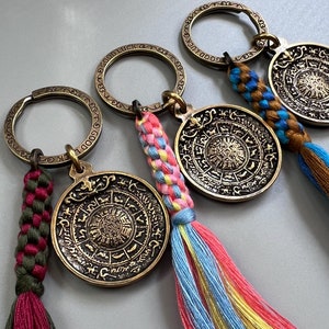 Puede incluir: Cuatro llaveros de oro con borlas de colores. Cada llavero presenta un dije redondo con un dise&ntilde;o intrincado y las palabras "Buena suerte" y "Buena fortuna".