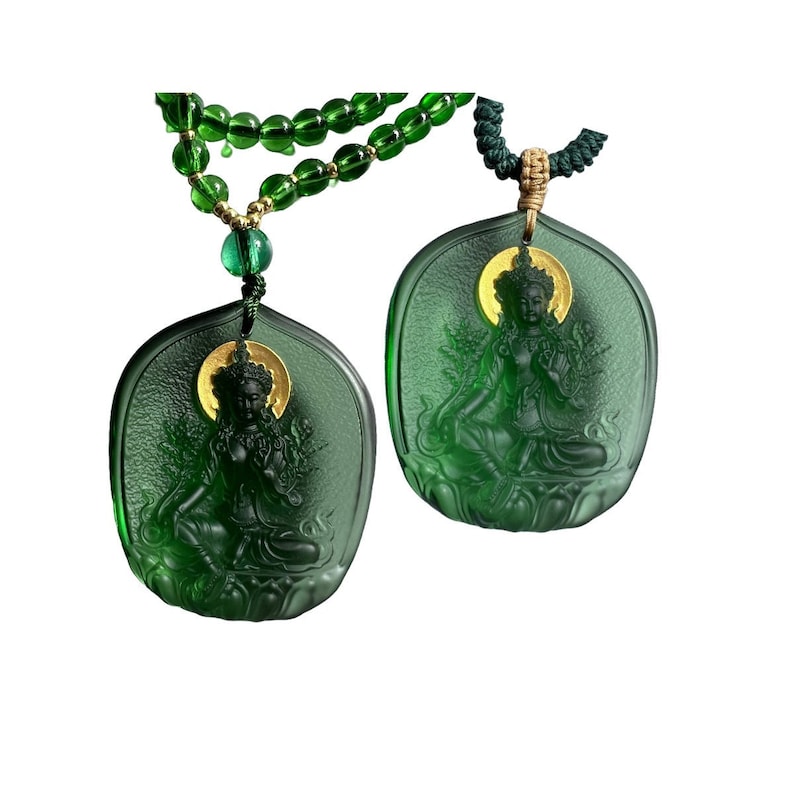 May include: A green glass necklace with two pendants featuring a carved image of a seated figure. The pendants have a gold halo around the figure's head. The necklace is made of green glass beads.