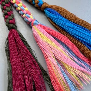 Puede incluir: Tres borlas trenzadas con hilos de colores. Las borlas est&aacute;n hechas de una variedad de colores, incluyendo verde, rojo, azul, amarillo y rosa.