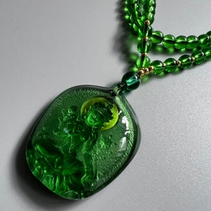 May include: A green jade necklace with a carved pendant featuring a figure of a deity. The pendant is intricately detailed and has a green and gold color scheme.