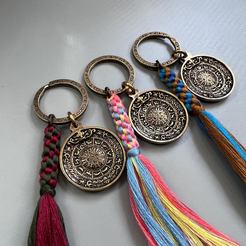 Puede incluir: Cuatro llaveros de oro con borlas de colores. Cada llavero presenta un dije redondo con un dise&ntilde;o intrincado y las palabras "Buena suerte" y "Buena fortuna".
