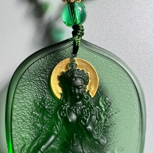 May include: Green glass pendant with a gold-colored halo around a carved image of a deity. The pendant is attached to a green beaded chain.