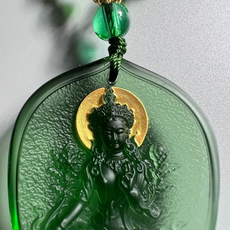 May include: Green glass pendant with a gold-colored halo around a carved image of a deity. The pendant is attached to a green beaded chain.