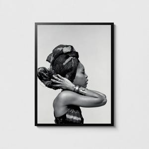 May include: Framed monochrome portrait of a person with a patterned head wrap and sleeveless top. Silver bracelets and rings adorn the person, whose hands are gently touching their neck. The image is in a black frame.