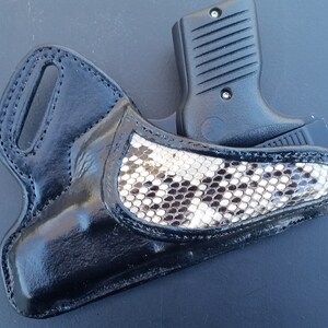 May include: Black leather holster with a snakeskin accent, holding a black handgun. The holster has a belt loop and a glossy finish. The snakeskin pattern is black, white, and grey.