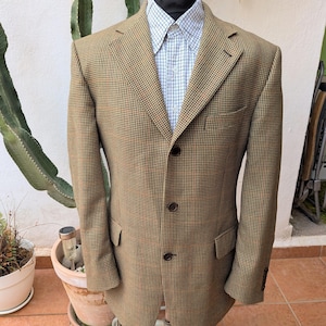 May include: A brown and tan houndstooth blazer featuring a notched lapel, three dark buttons down the front, and two flap pockets. The blazer is worn over a light blue and white grid-patterned button-down shirt with a pointed collar.
